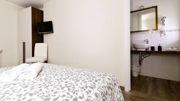 Ein Hotelzimmer mit Bett, Wand-Fernseher, Badezimmer mit Waschbecken, Spiegel und Fön.