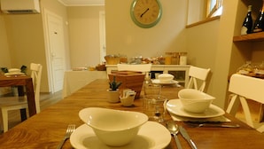 Un coin repas avec une table en bois mise pour un repas, comprenant des bols, des assiettes, des couverts et une horloge au mur.