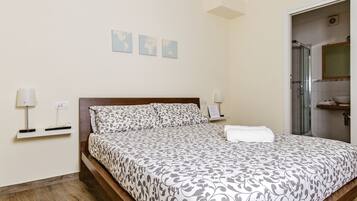 A neatly made bed with patterned bedding, a bedside table with a lamp, and a wall-mounted shelf with a phone and a small item.