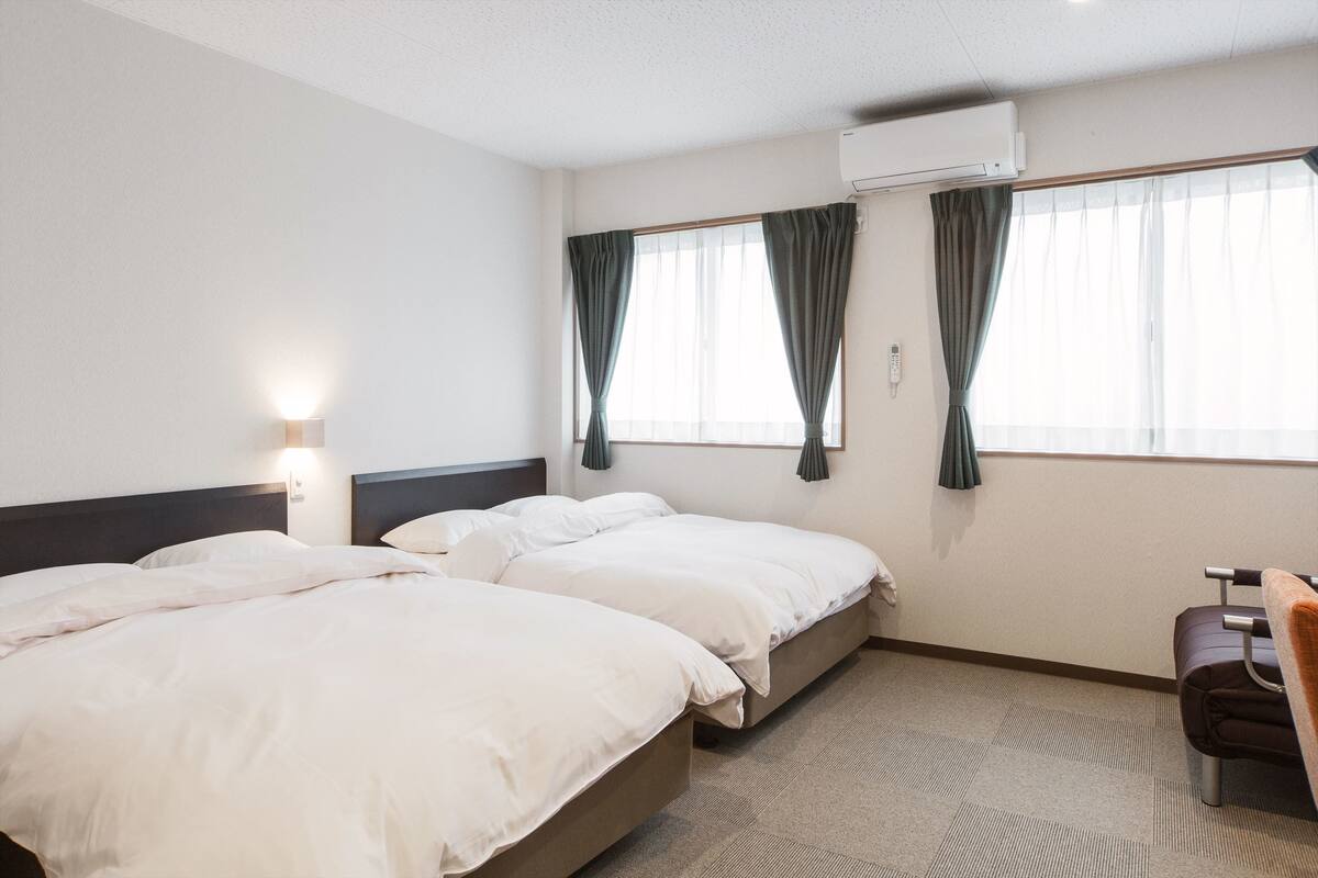 A hotel room with two beds, a desk, and a chair.