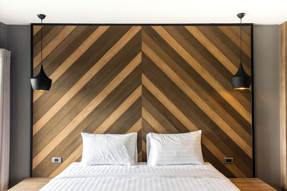 A modern bedroom with a chevron-patterned wooden headboard, two bedside lamps, and a neatly made bed with white linens.