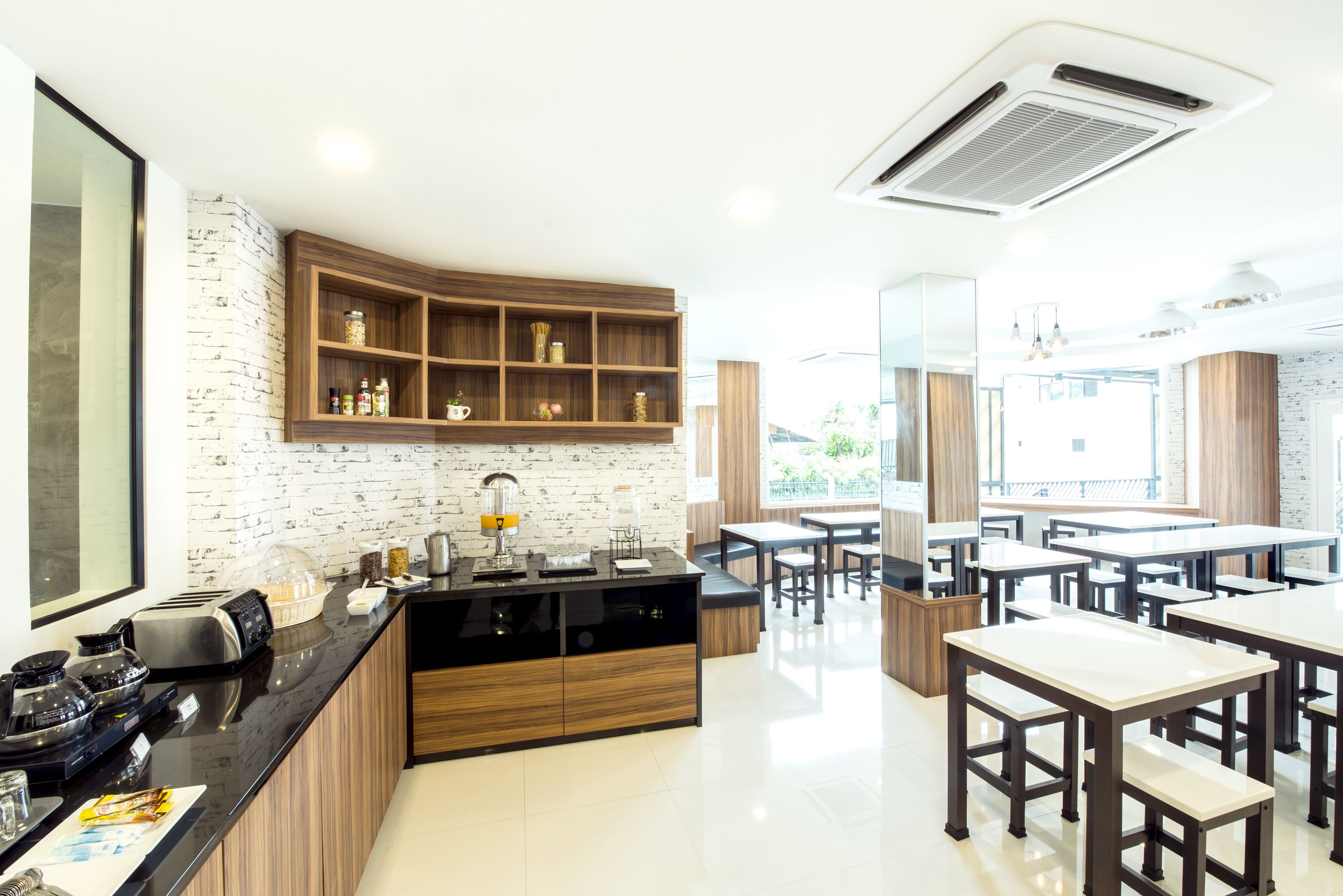 Una cocina moderna con encimera negra, armarios de madera y pared de ladrillo. Hay varias mesas y sillas en el comedor.