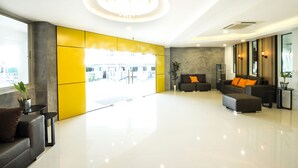 A modern lobby with a large window, a chandelier, and a seating area with a sofa and armchairs. - The Circle Hotel (Buriram)