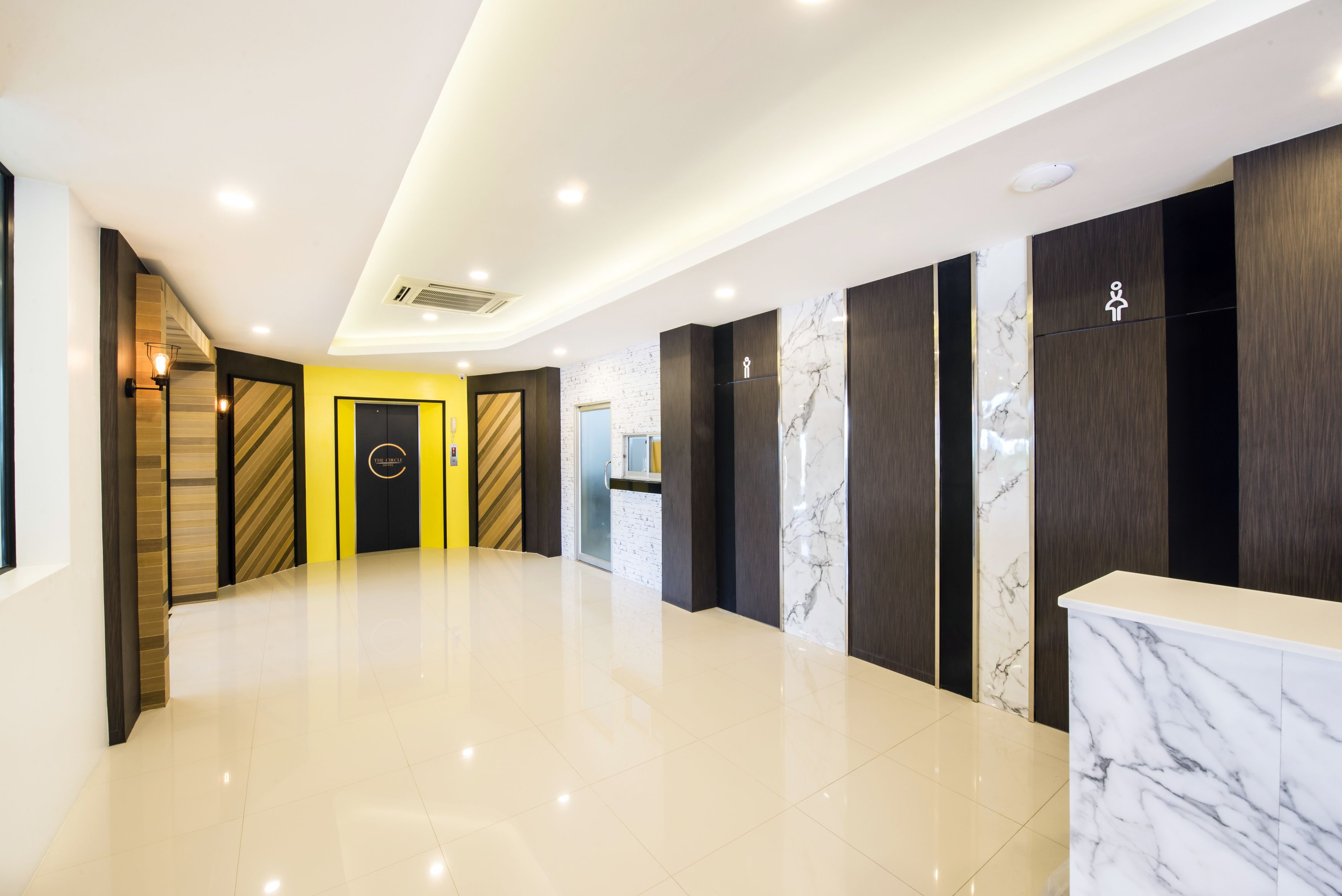 Un moderno vestíbulo de hotel con piso limpio y pulido, una mesa de recepción y una pared amarilla con una puerta.