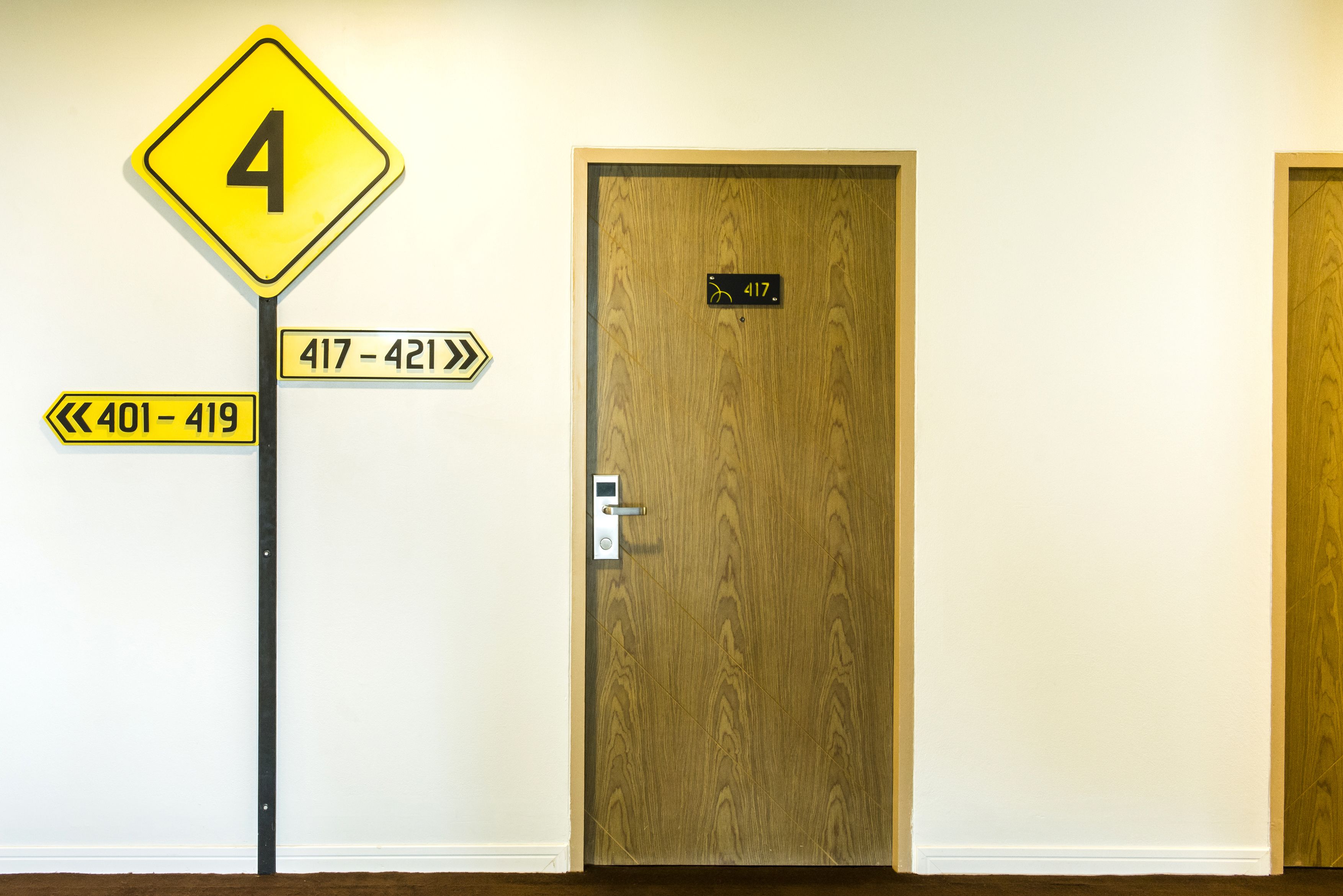 A hotel room with a wooden door, a number sign indicating room 417, and directional signs for room numbers 401-419 and 417-421.