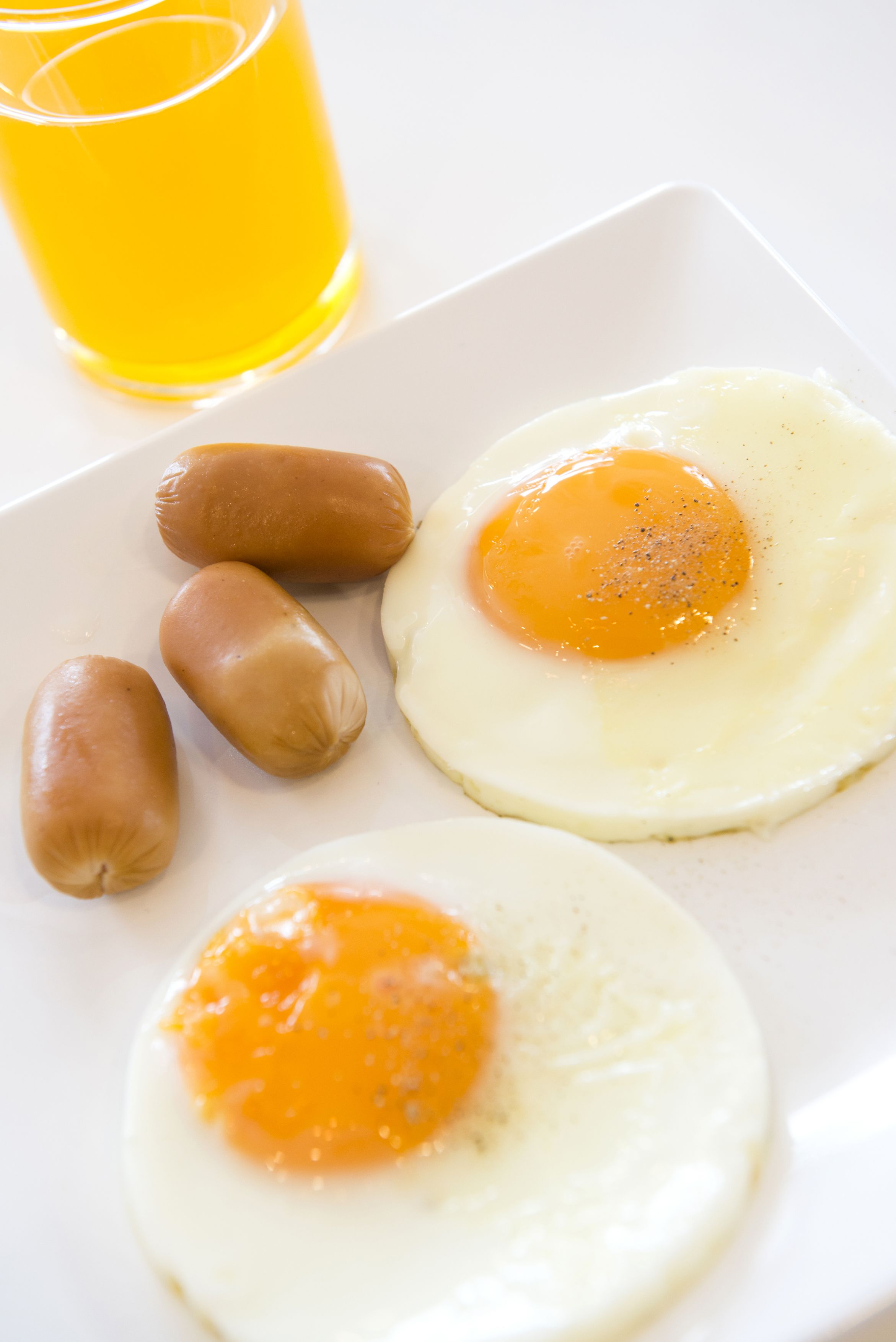 A white plate with two sunny-side-up eggs and three sausages.