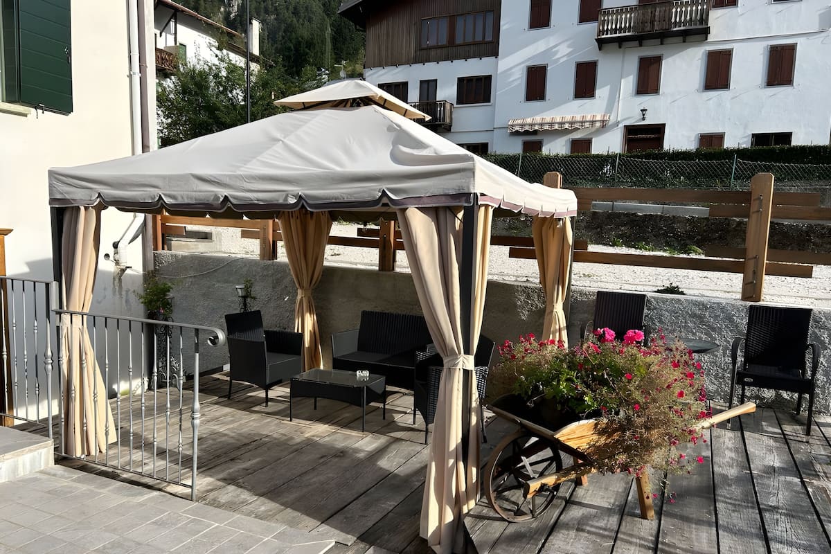 Un espacio de estar al aire libre cubierto con una mesa, sillas, una planta en maceta y un carrito de madera.