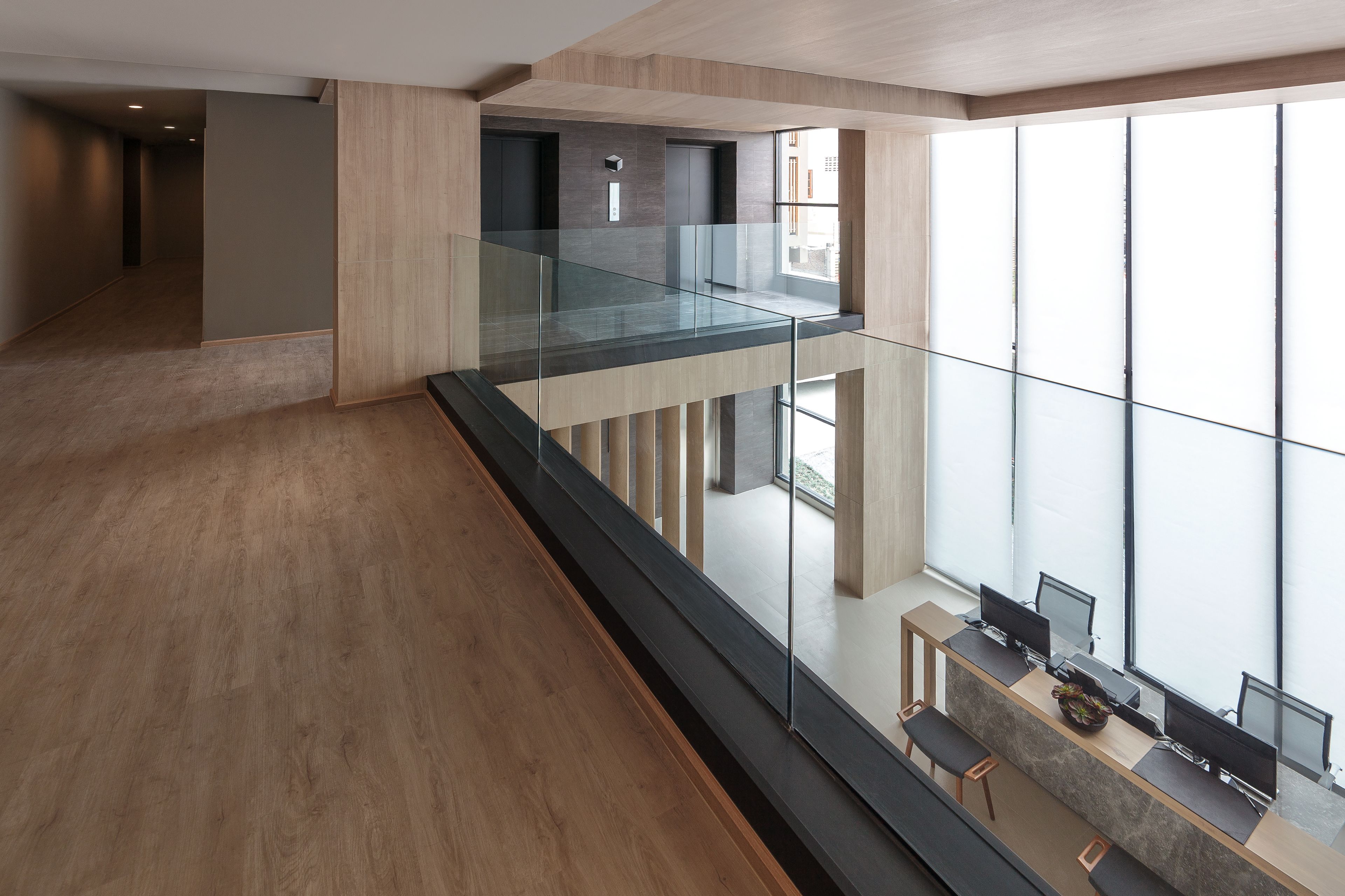 Un interior moderno con barandilla de cristal, suelo de madera y un escritorio con computadoras.