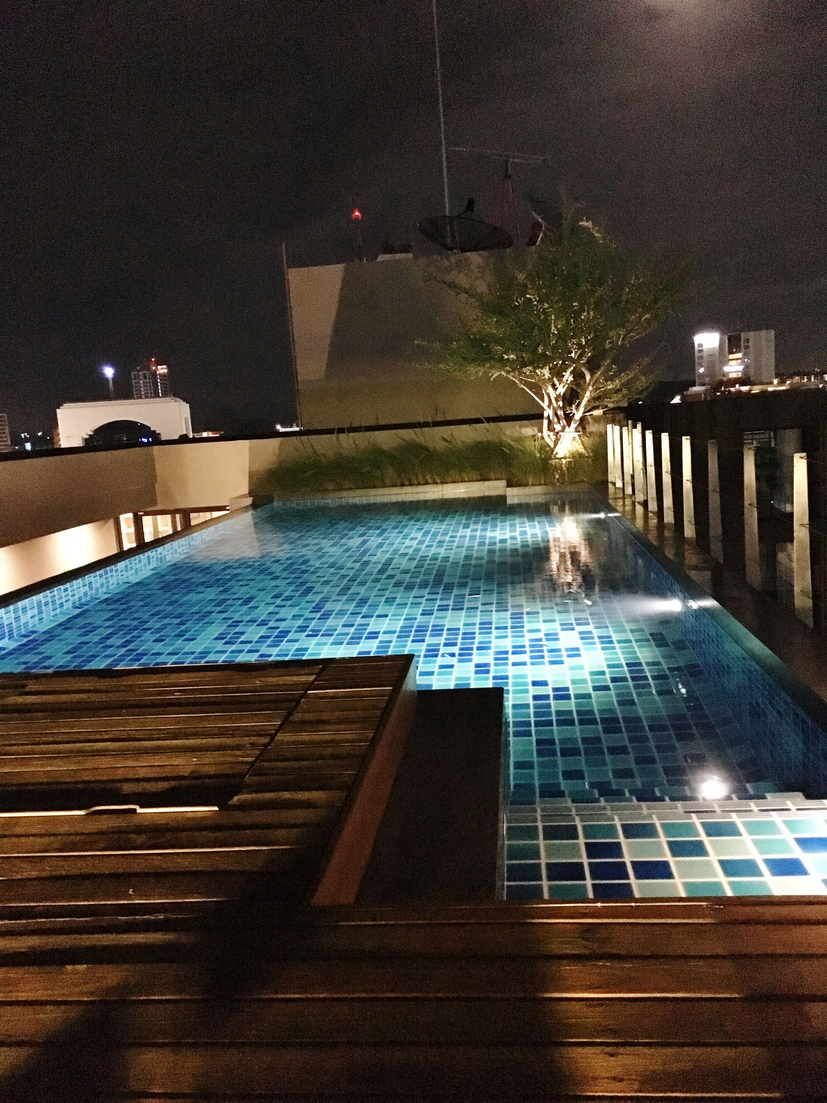 A nighttime swimming pool with tiled flooring and wooden deck.