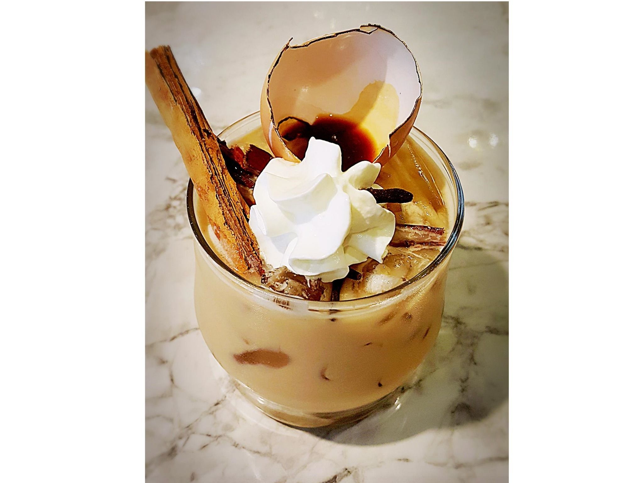 A dessert in a glass with whipped cream, a chocolate shell, and a cinnamon stick.