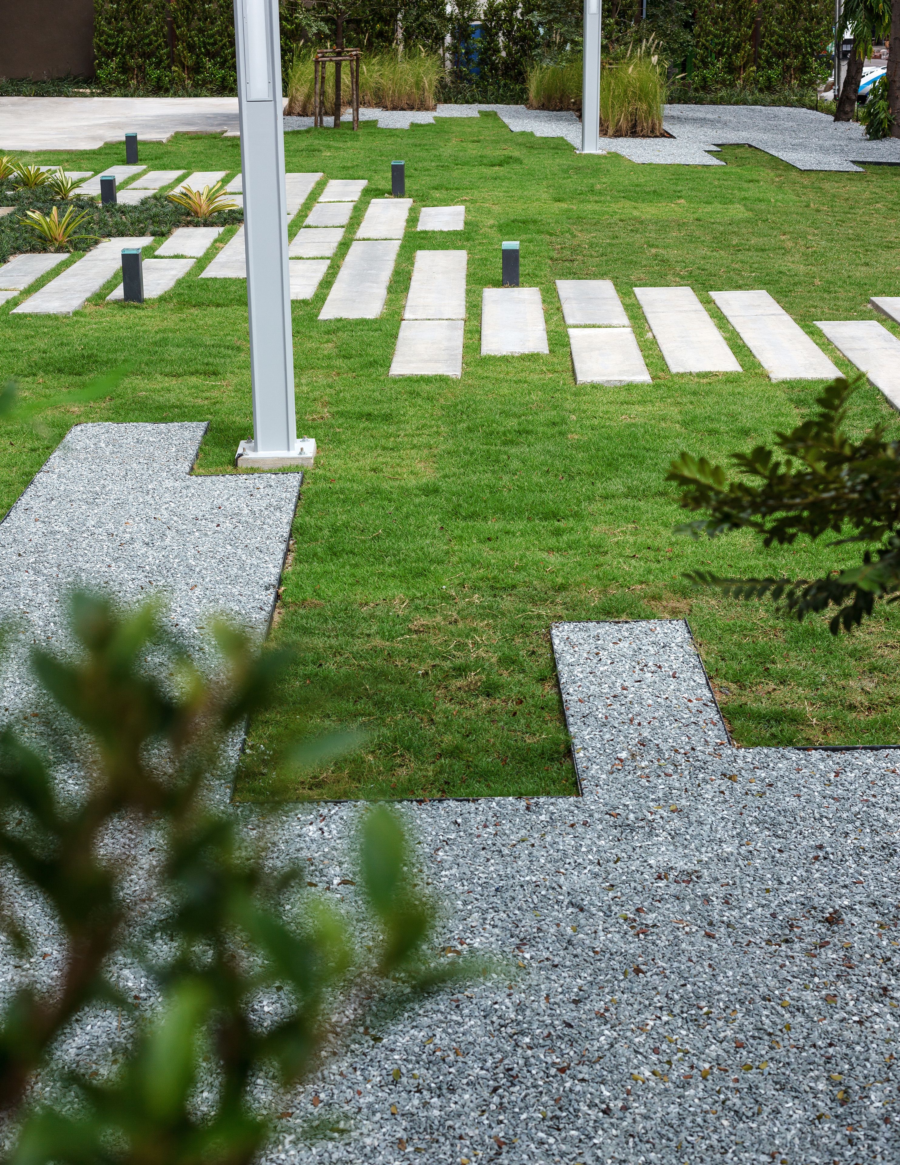 A landscaped garden with a cross-shaped gravel path, surrounded by grass and small plants.