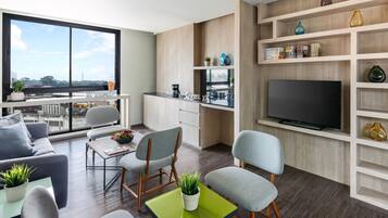 A modern living room with a sofa, chairs, a coffee table, and a TV. There's a balcony with a view of the city.