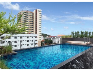 A swimming pool with a clear blue water, surrounded by a modern building with multiple floors and balconies. - Madera Residence Siracha (Si Racha)