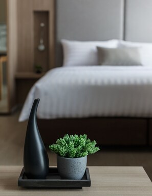 A modern bedroom with a neatly made bed, a small potted plant on a tray, and a black vase on the nightstand. - Madera Residence Siracha (Si Racha)