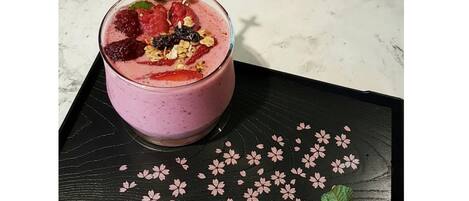 Un bicchiere di smoothie con fragole e menta su un vassoio nero decorato con fiori di ciliegio.