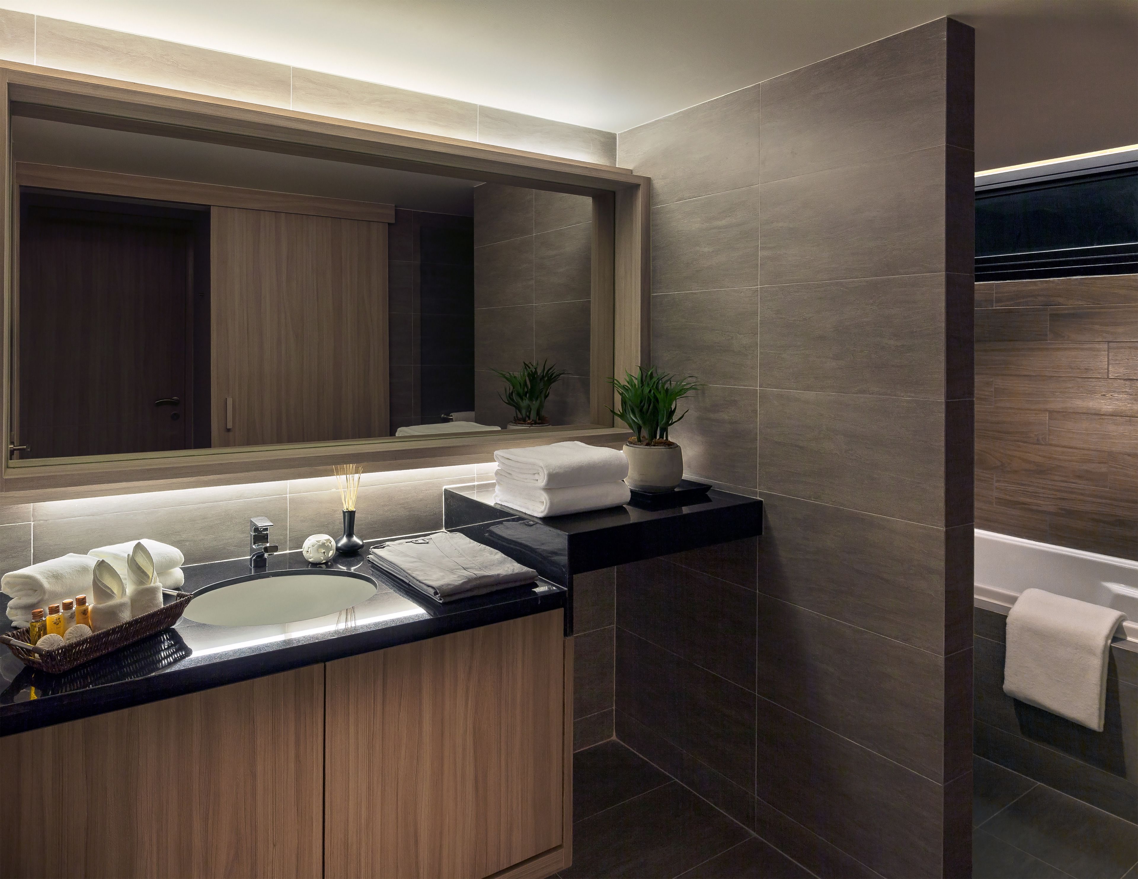 A modern bathroom with a large mirror, dark tiles, a wooden vanity, and a towel rack.