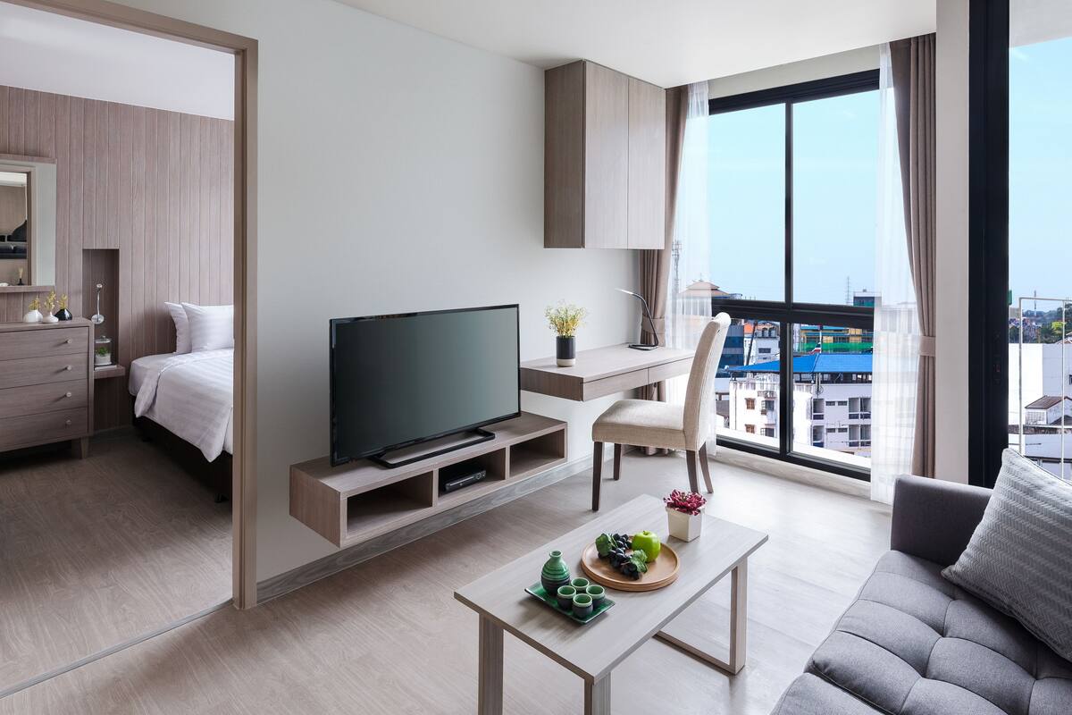 Ein modernes Hotelzimmer mit Bett, Fernseher, Schreibtisch und einem Balkon mit Blick auf die Stadt.