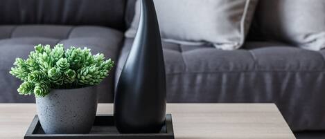Un salon moderne avec un canapé gris, une petite plante en pot et un vase noir posé sur une table basse en bois.