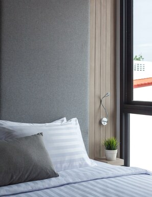 A modern bedroom with a bed, grey textured wall, wooden paneling, a window with a view, and a small potted plant. - Madera Residence Siracha (Si Racha)