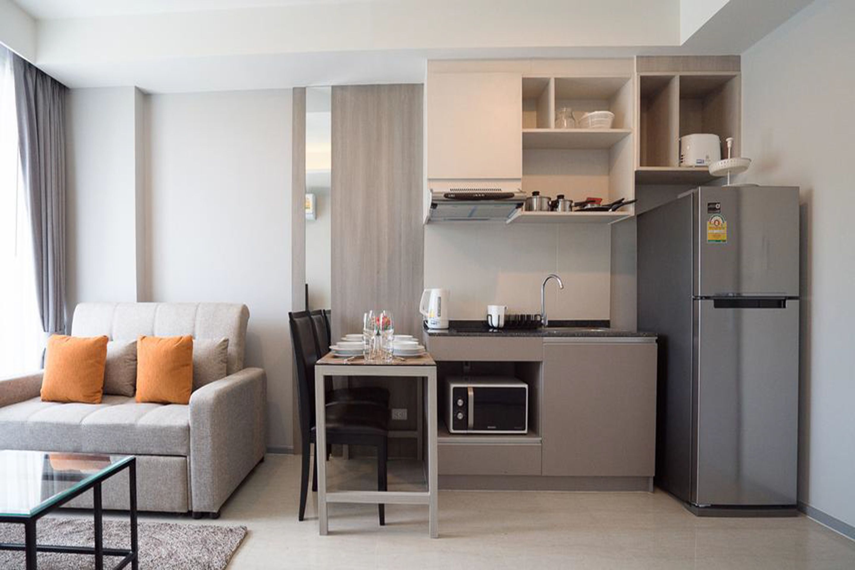 A compact living space with a kitchenette, a sofa with orange cushions, a dining table, and a modern refrigerator.