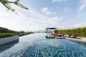 A infinity pool with lounge chairs and a pergola, surrounded by greenery and overlooking a scenic landscape. - 6th Avenue Surin Beach (Choeng Thale)