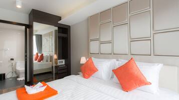 Habitación de hotel con una cama grande, dos almohadas naranjas, un cabecero blanco y un espejo que refleja la habitación.