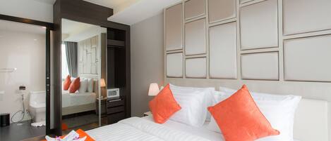 A hotel room with a large bed, two orange pillows, a white headboard, and a mirror reflecting the room.