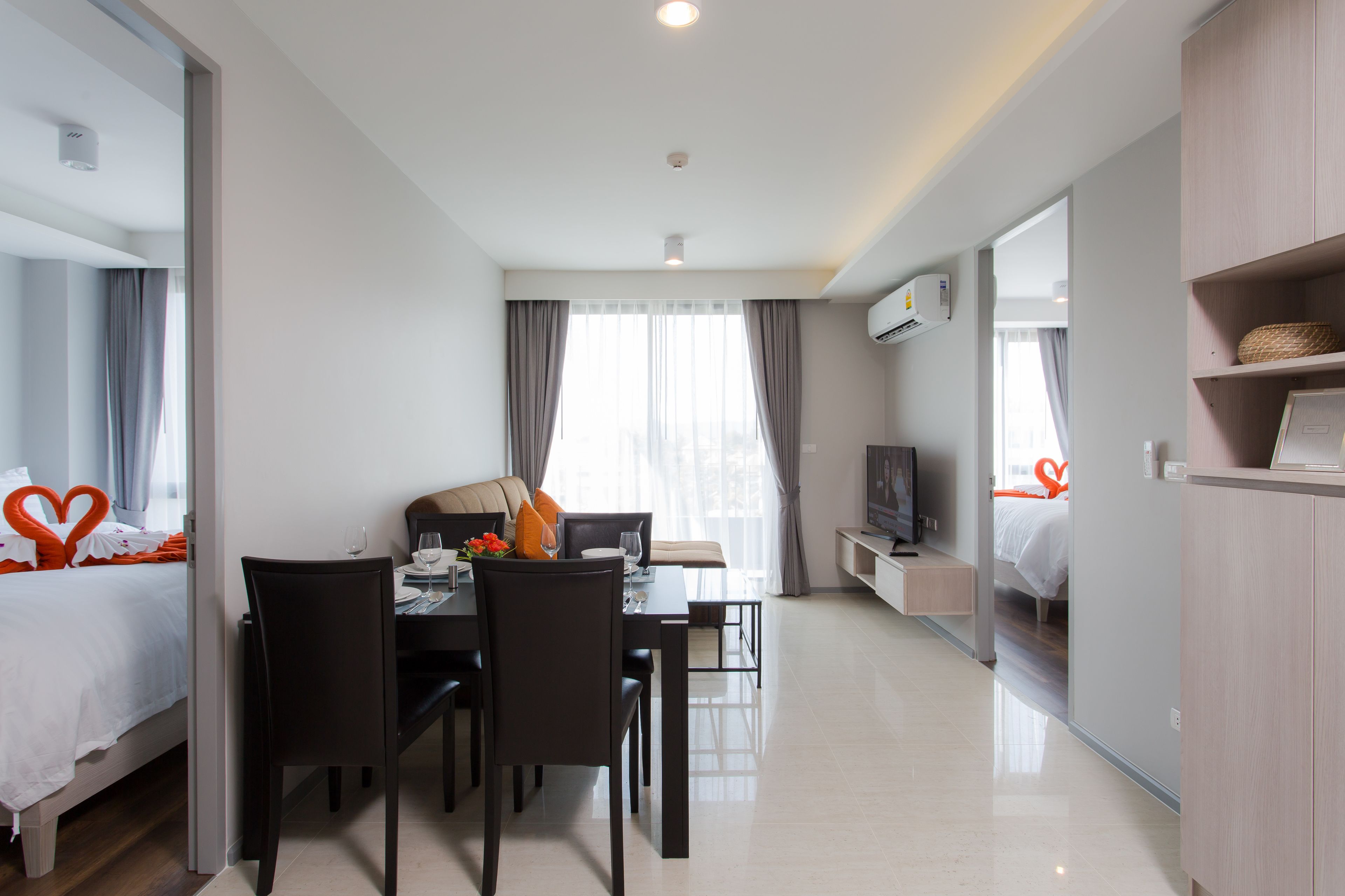 A modern hotel room with a bed, a dining area with a table and chairs, a TV, and a large window with curtains.