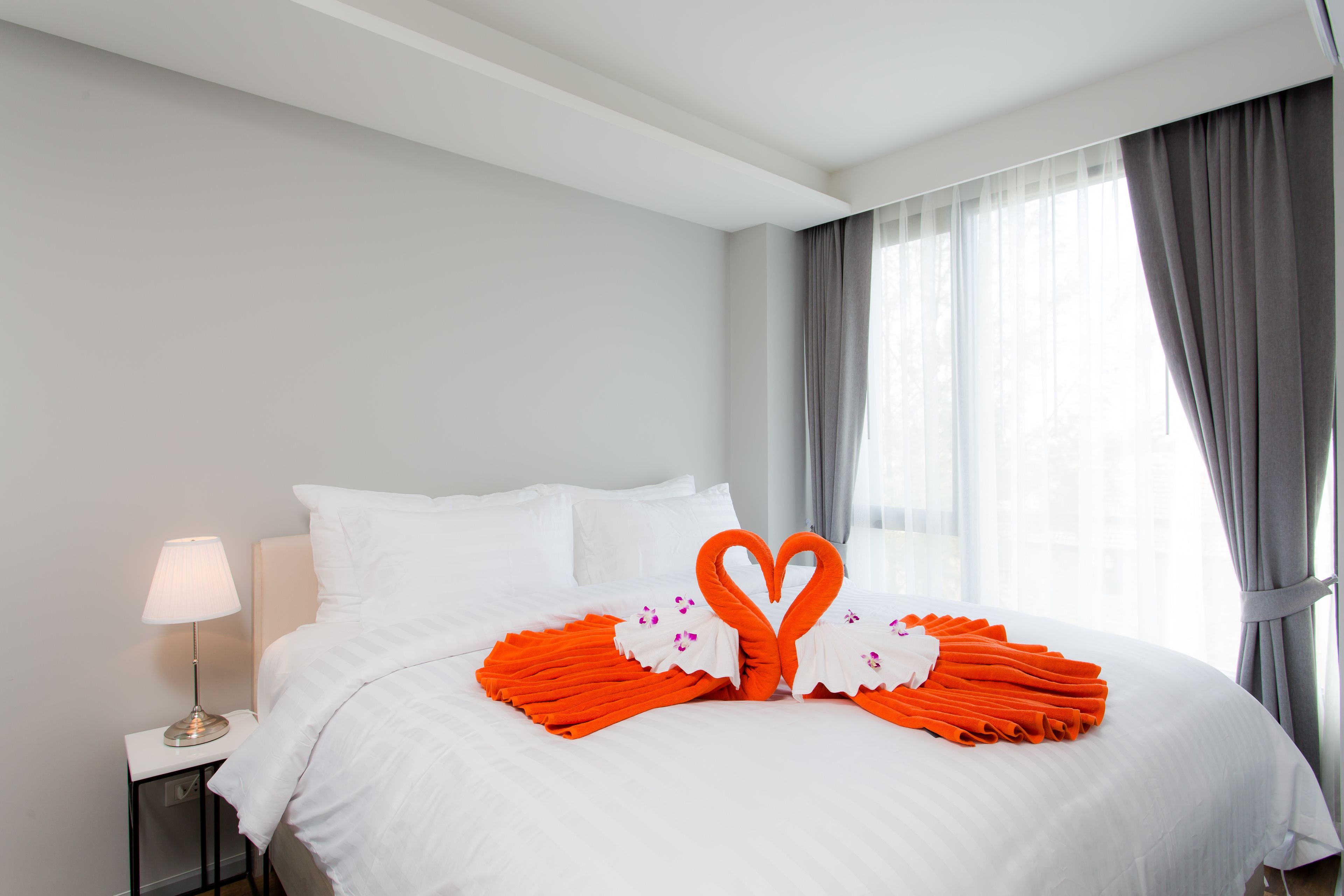 A neatly made bed with white linens and orange towels arranged in heart shapes.