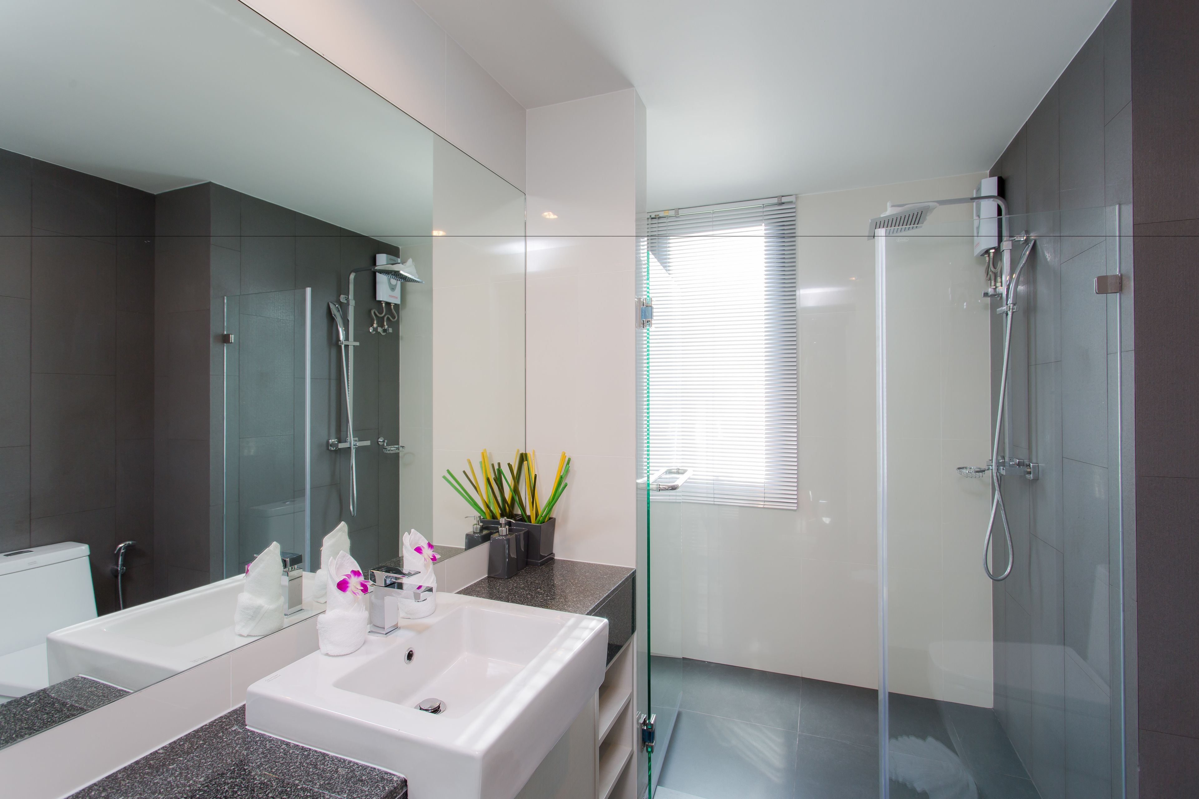 Un baño moderno con ducha de vidrio, un espejo grande y encimera de granito.