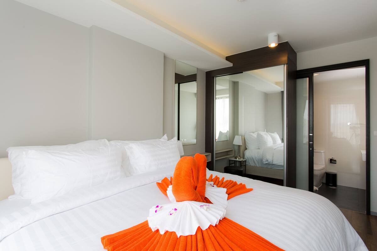 Quarto de hotel com cama grande, espelho, mesa de cabeceira e porta para o banheiro.