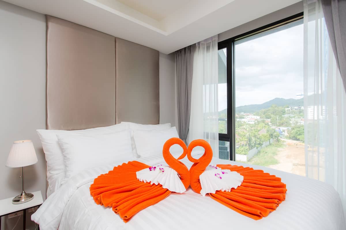 Quarto de hotel com uma cama grande, roupa de cama branca e toalhas laranja dispostas em formato de coração.