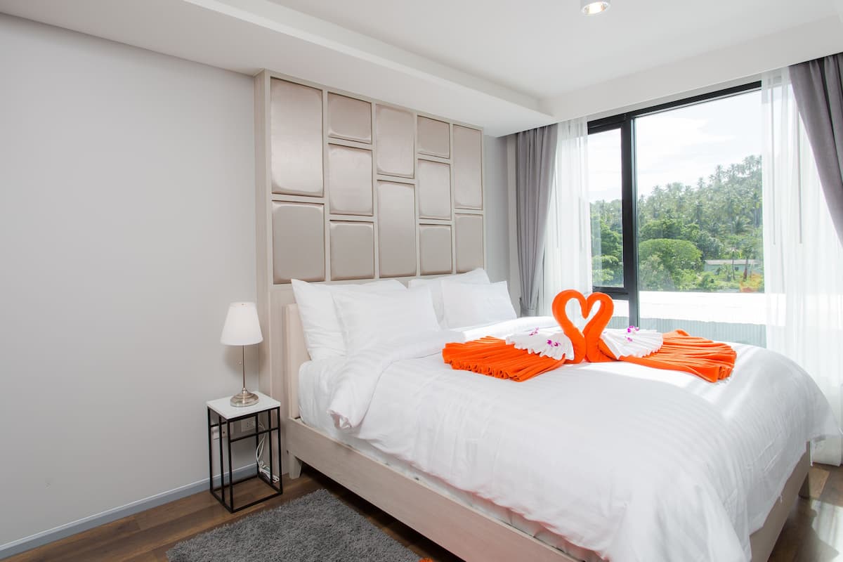 Quarto de hotel moderno com uma cama grande, uma mesa de cabeceira e vista para o verde lá fora.