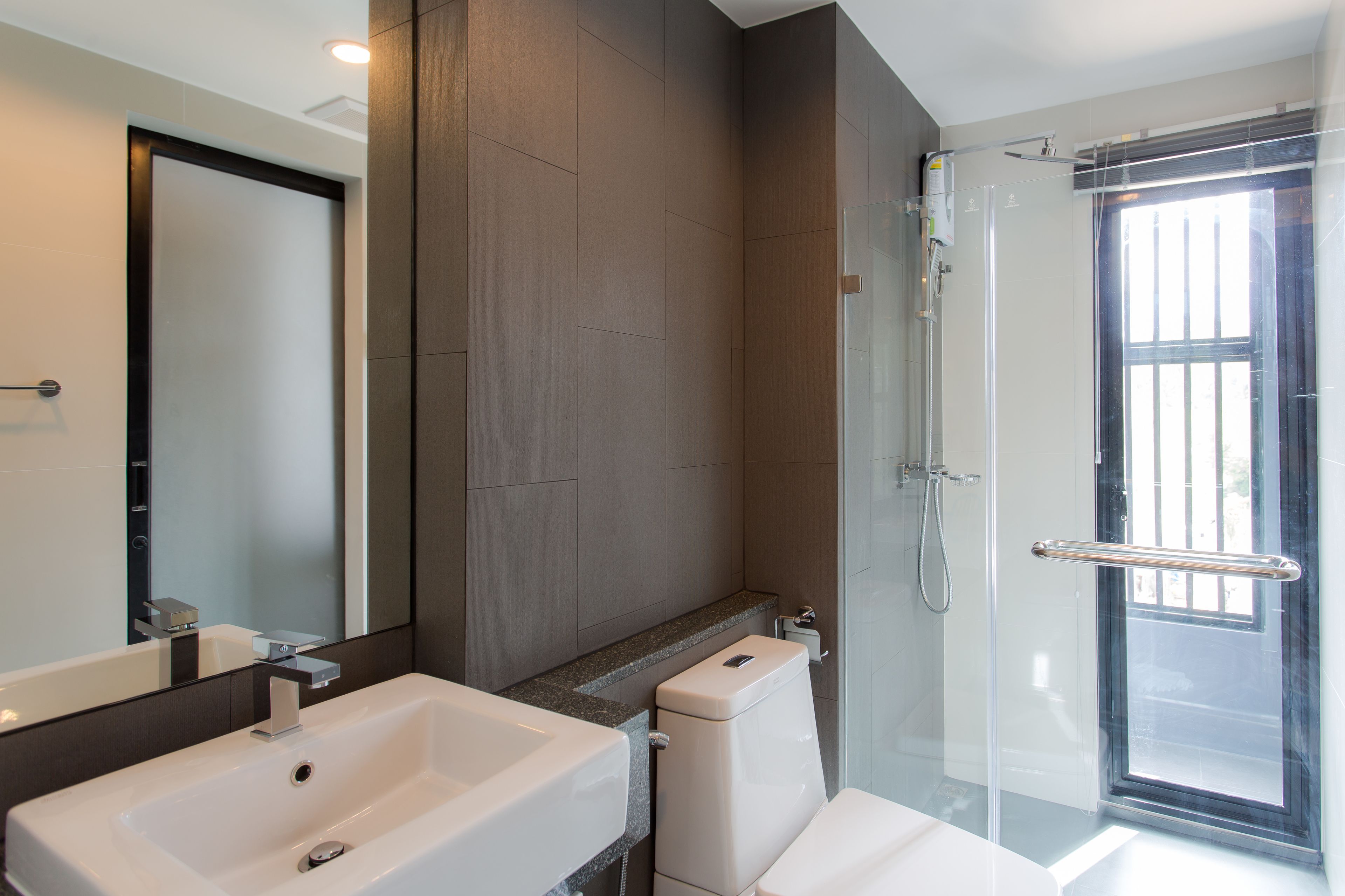 A modern bathroom with a large mirror, a white sink, a toilet, and a glass shower enclosure.