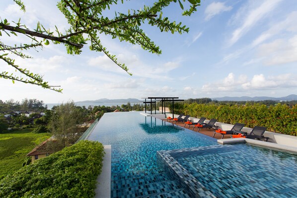 Une piscine à débordement offrant une vue sur les montagnes et un espace jardin aménagé avec des chaises longues.