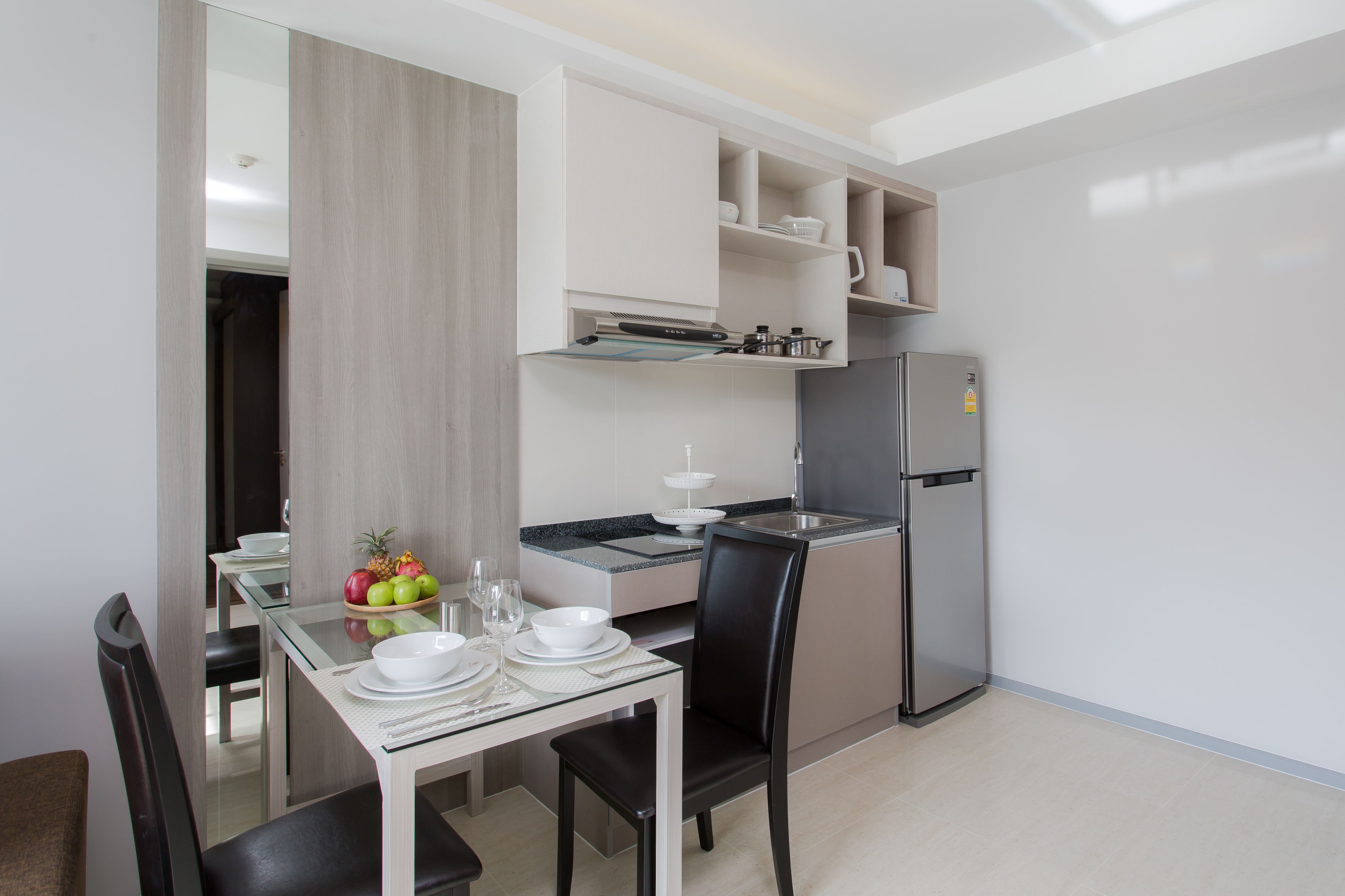 A modern kitchen with a dining area, including a glass table, chairs, and a refrigerator.