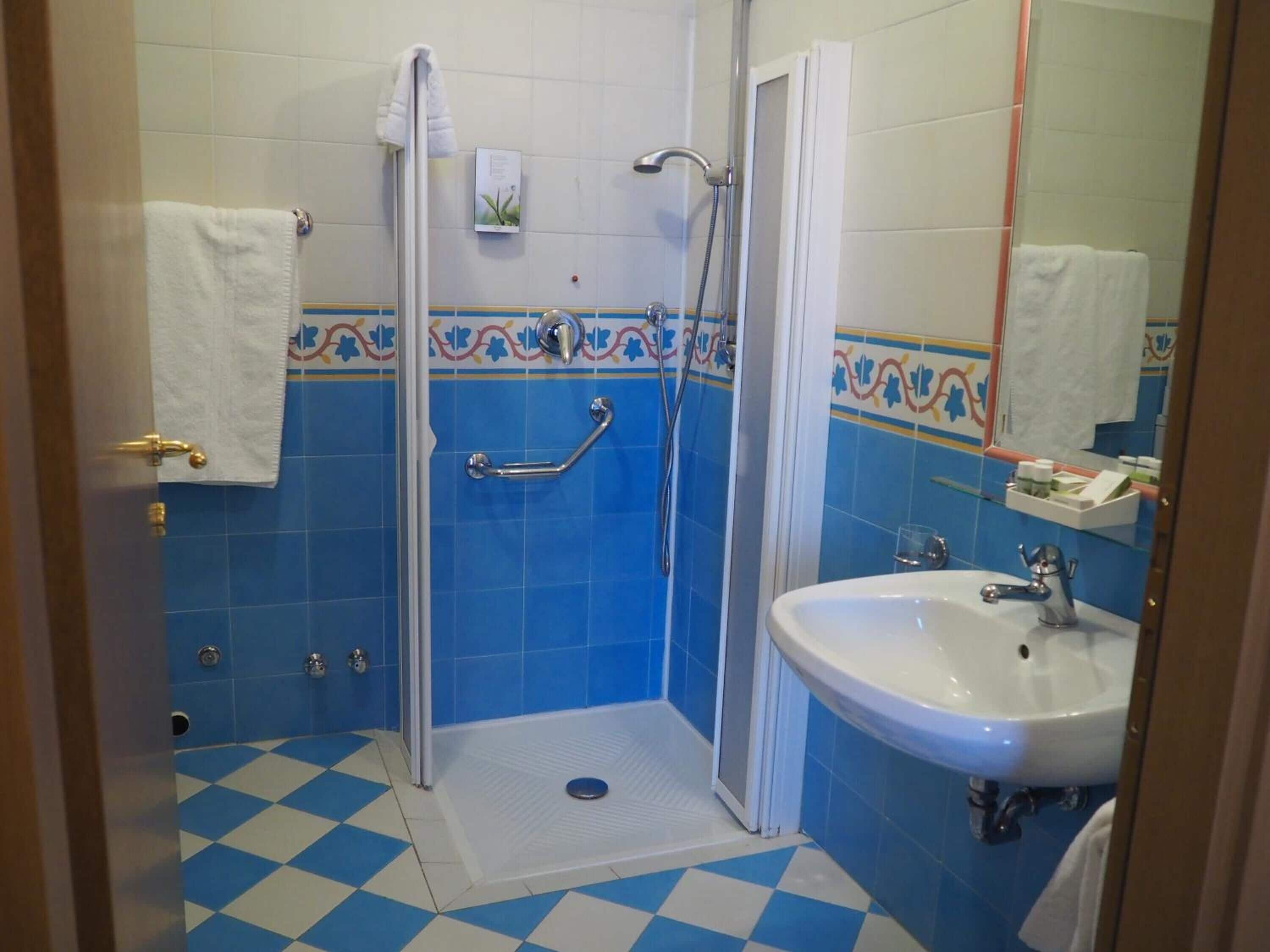 Un baño con ducha, lavamanos y barra de apoyo.