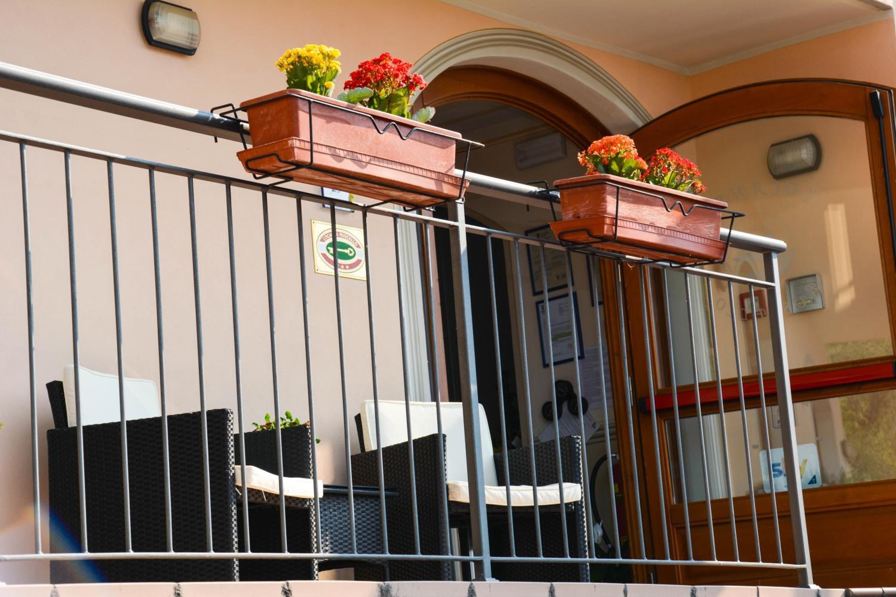 A balcony with two wicker chairs and two terracotta flower pots with flowers.