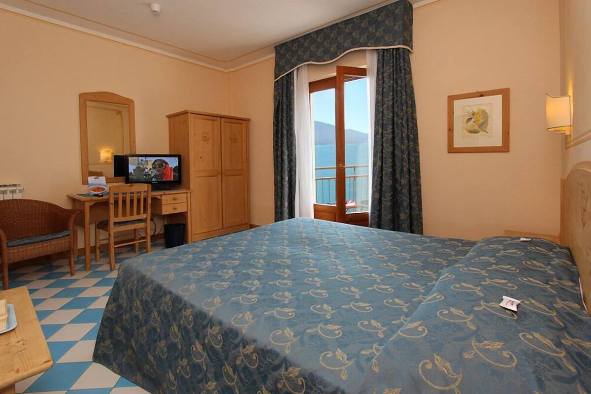 A hotel room with a bed, a desk with a television, a chair, a wardrobe, and a window with a view.