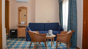 A room with a blue sofa, two wicker chairs, a small round table with a kettle, a wooden cabinet, and a mirror. - Hotel Locanda Ruscello Garnì (Limone sul Garda)