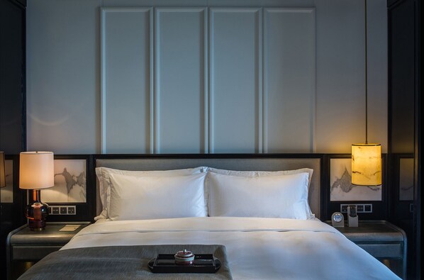 A hotel room with a large bed, two bedside lamps, a nightstand with a clock, and a tray with a camera. -  Hangzhou Jiutai Hotel (Hangzhou)