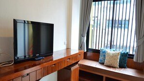 Una sala de estar moderna con un televisor de pantalla plana sobre un mueble de madera, un banco empotrado con cojines y un ventanal con persianas.