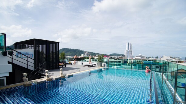 Una piscina infinita en la azotea con baldosas azules cristalinas, barandilla de cristal y una estructura de edificio moderno al fondo.