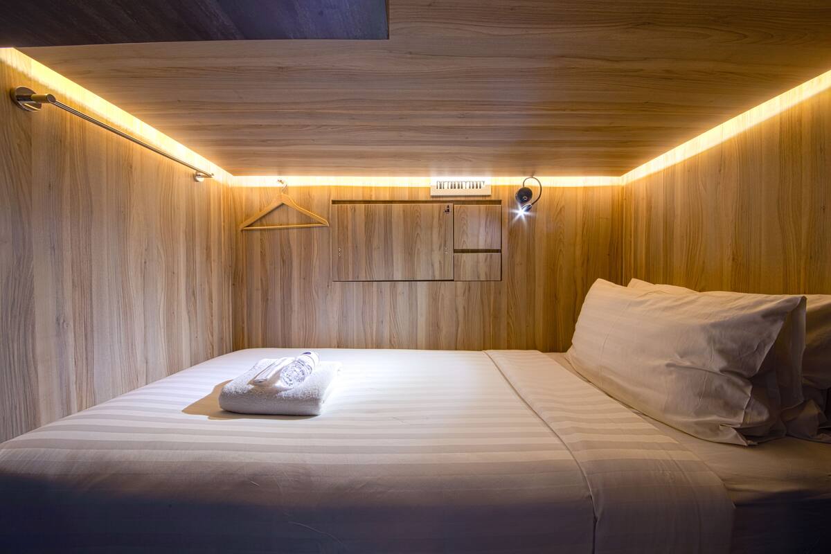 Cama bem arrumada com toalha, paredes de painel de madeira e luminária pendente.