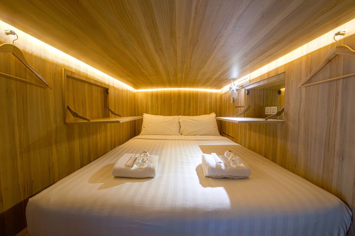 Quarto de hotel com teto de madeira, uma cama grande com roupa de cama branca e um espelho na parede.