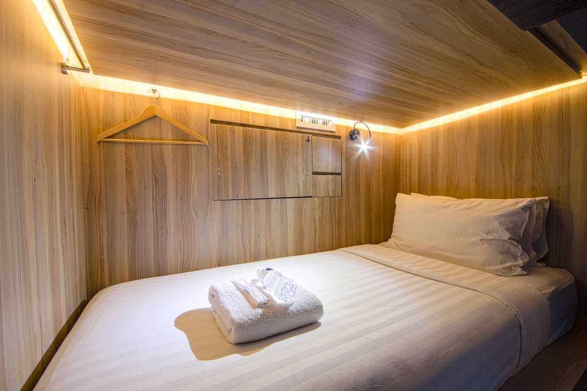 Cama bem arrumada com toalha e um cabideiro pendurado em parede de madeira.
