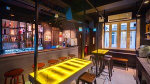Een bar met een lange, verlichte toog, krukken en flessenkasten.