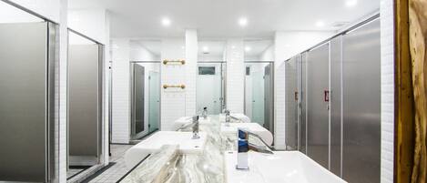 Une salle de bain moderne dotée de plusieurs lavabos, d’un comptoir en marbre et d’une cabine de douche en verre.