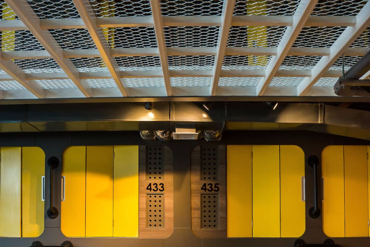 A row of yellow lockers with numbers 432 to 438, a metal rack, and a wooden floor.