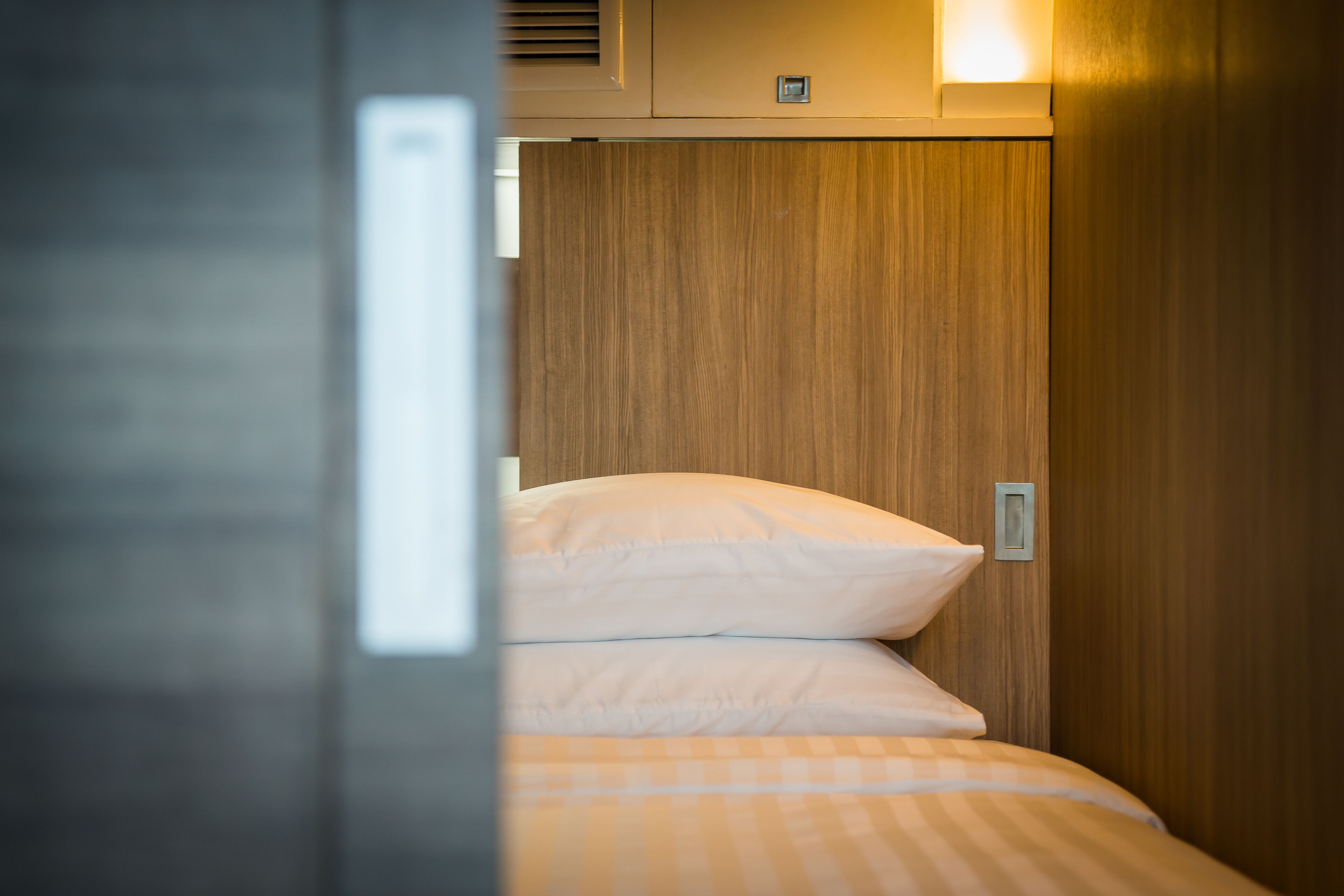 A narrow, wooden-paneled room with a bed featuring white and orange checkered bedding.